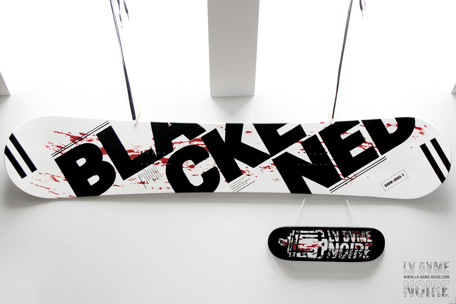 Main view of the snowboard and Tiny-skateboard painted in black, white, red, and the word Blackened in big bold letters